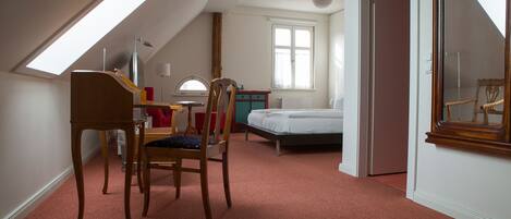 A bedroom with a sloped ceiling, a bed, a chair, a desk, and a window.