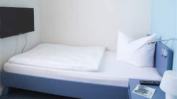 Un lit simple avec une literie blanche, un téléviseur à écran plat fixé au mur, une table de chevet avec une lampe et une télécommande.