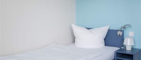 A single bed with white bedding, a nightstand with a lamp, and a wall-mounted alarm clock.