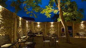 Un espace extérieur aménagé en patio, avec des murs en briques, des tables, des chaises et un arbre.