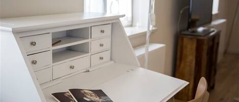 A white desk with drawers and a magazine on it. There is a chair in front of the desk.