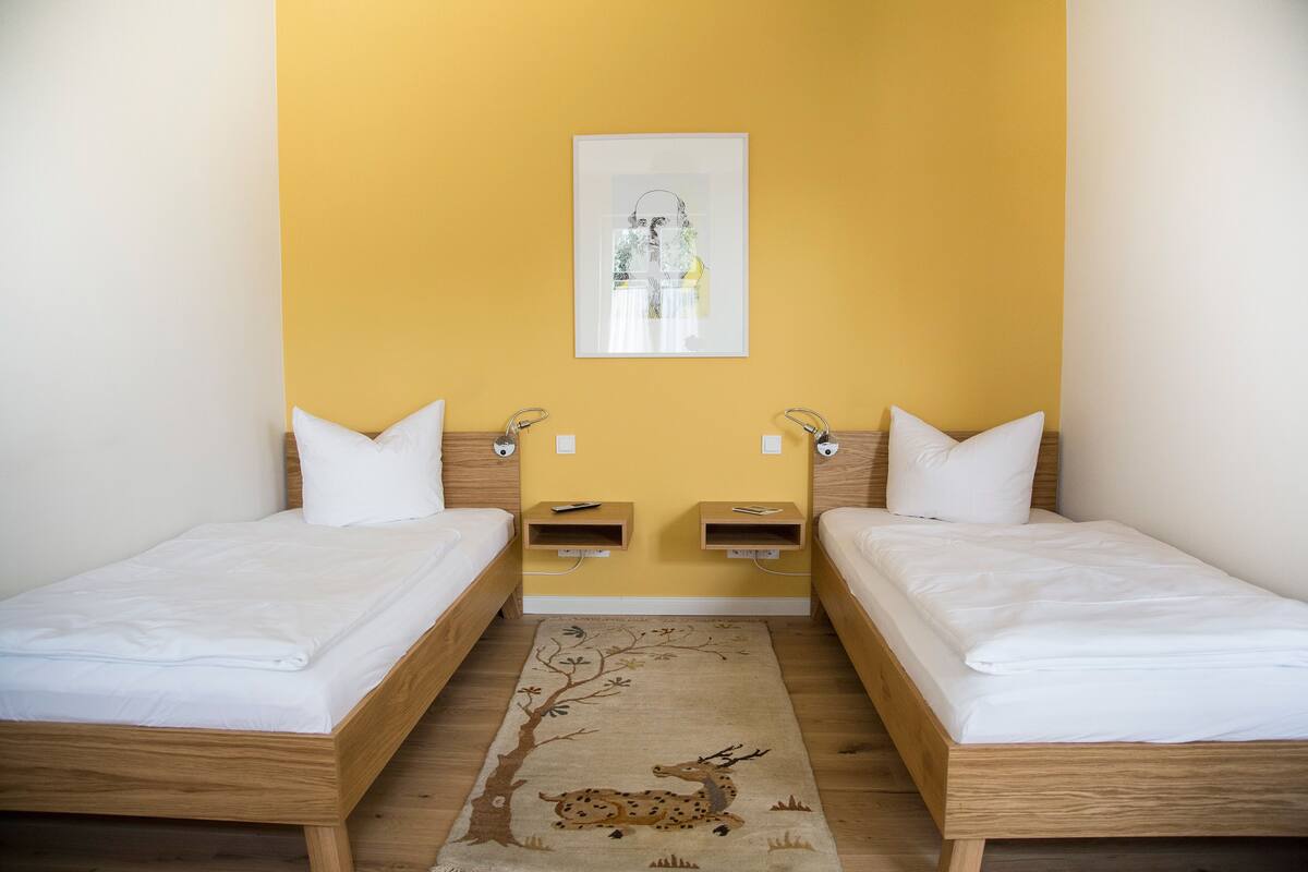 Une chambre avec deux lits simples, une tête de lit en bois, un tapis orné d’un motif de cerf et un tableau accroché au mur.