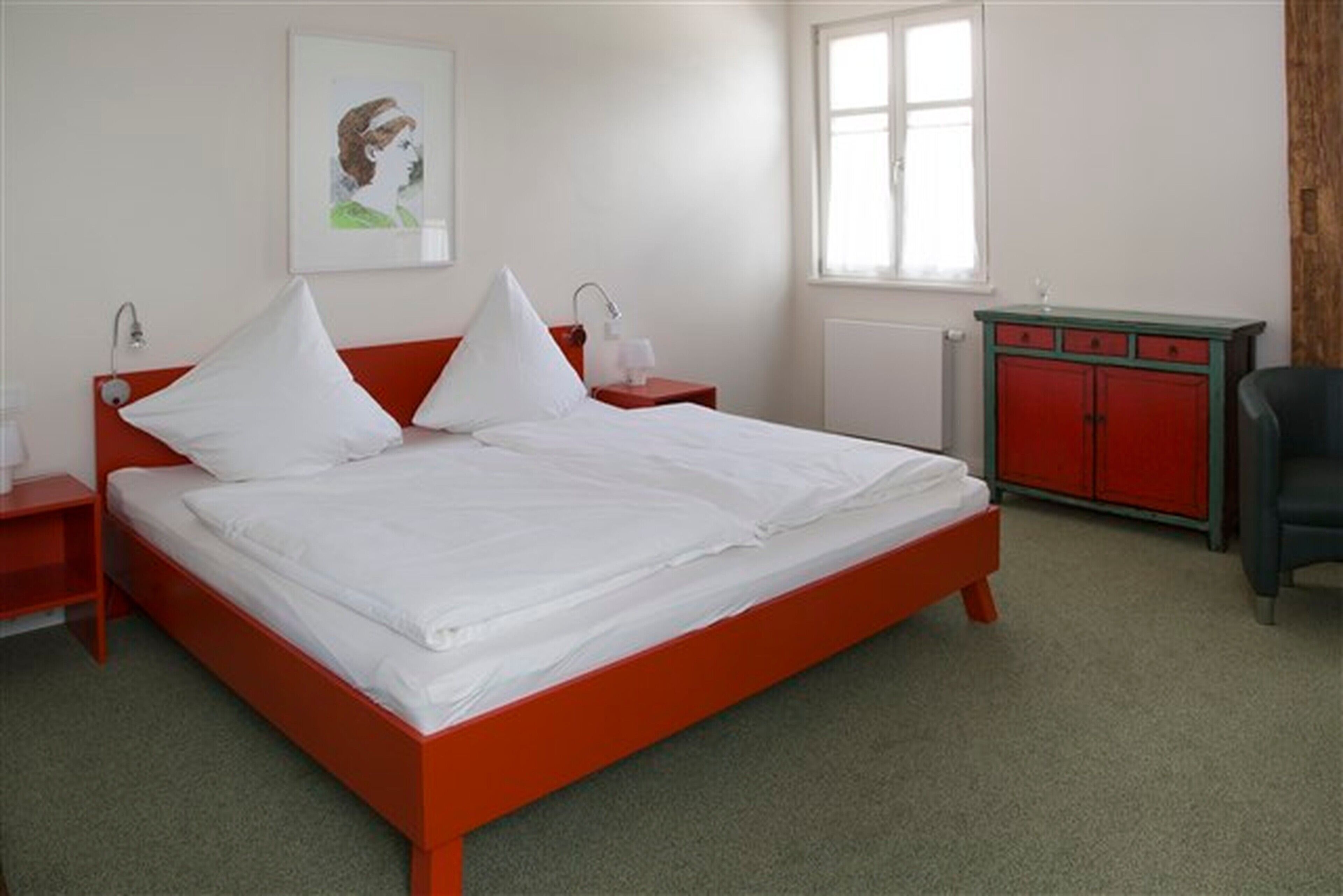 Una cama con estructura roja, ropa de cama blanca y dos mesitas de noche con lámparas.