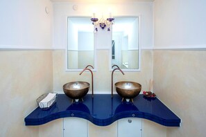 Un baño con dos lavamanos de cobre sobre un mostrador azul, un espejo arriba y una araña.