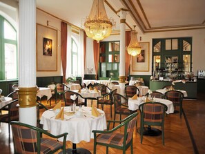 Un restaurant avec des tables rondes, des chaises vertes et des lustres.