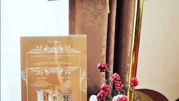 A table with a brass desk lamp, a framed informational card, and a small vase with white flowers and red berries.