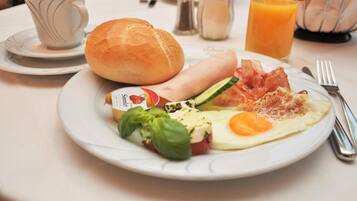 A breakfast plate with eggs, bacon, ham, cheese, tomato, and basil.