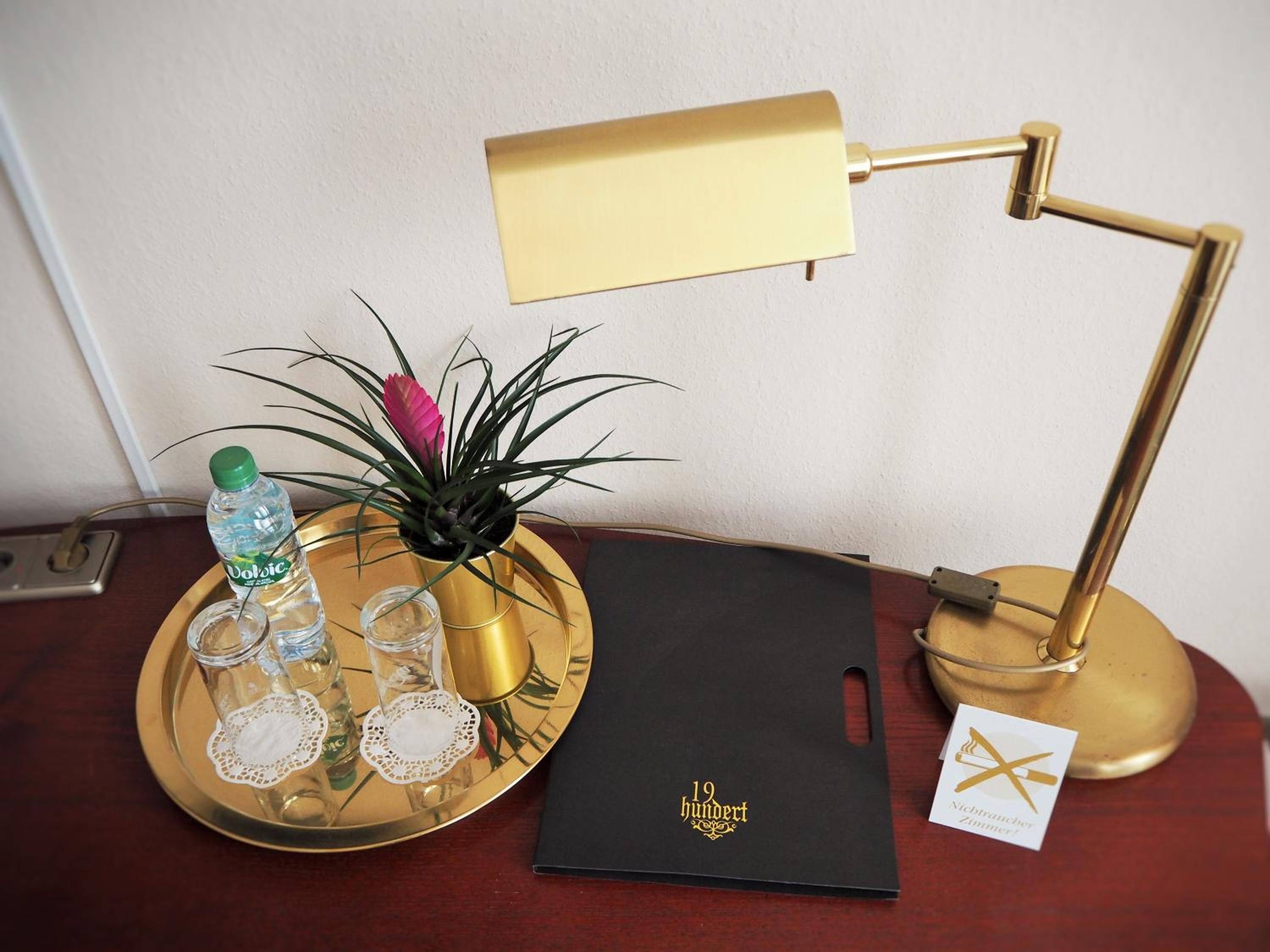 A desk with a gold desk lamp, a tray with a bottle, glasses, and a plant.