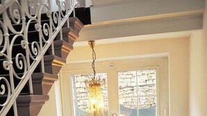 A staircase with a chandelier, a double door with windows, and two small tables with vases. - Gala Hotel (Pforzheim)