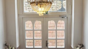 A grand entrance with a large, ornate chandelier, a double door with brick patterns, and a view of the outdoors through the windows. - Gala Hotel (Pforzheim)
