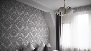 A modern hotel room with a patterned wallpaper, a bed with white linens, a bedside lamp, and a view of the outdoors through sheer curtains. - Gala Hotel (Pforzheim)
