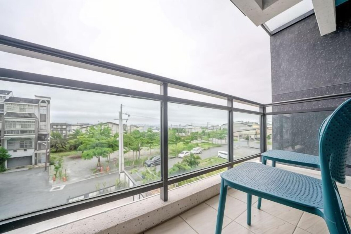 A balcony with a view of a cityscape, a metal railing, and a green chair.