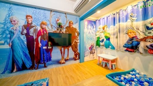 Una sala de juegos infantil con un mural temático de Frozen, una televisión y una piscina de pelotas.