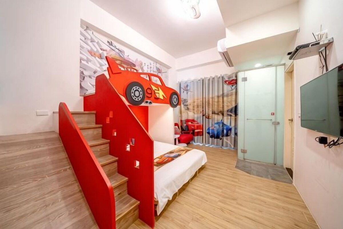 A bedroom with a bunk bed, a red car-shaped headboard, a television, and a sliding door.