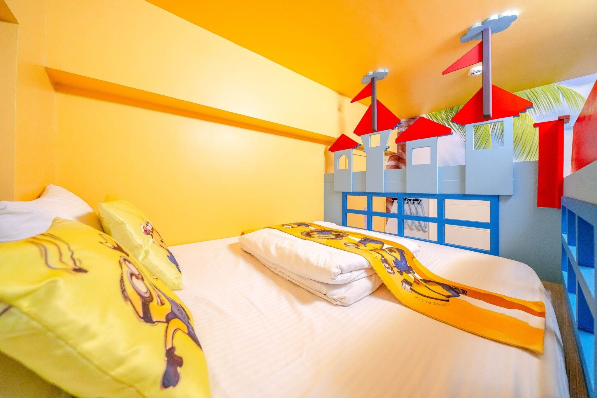 A hotel room with a bed, pillows, and a blue and red playhouse structure.