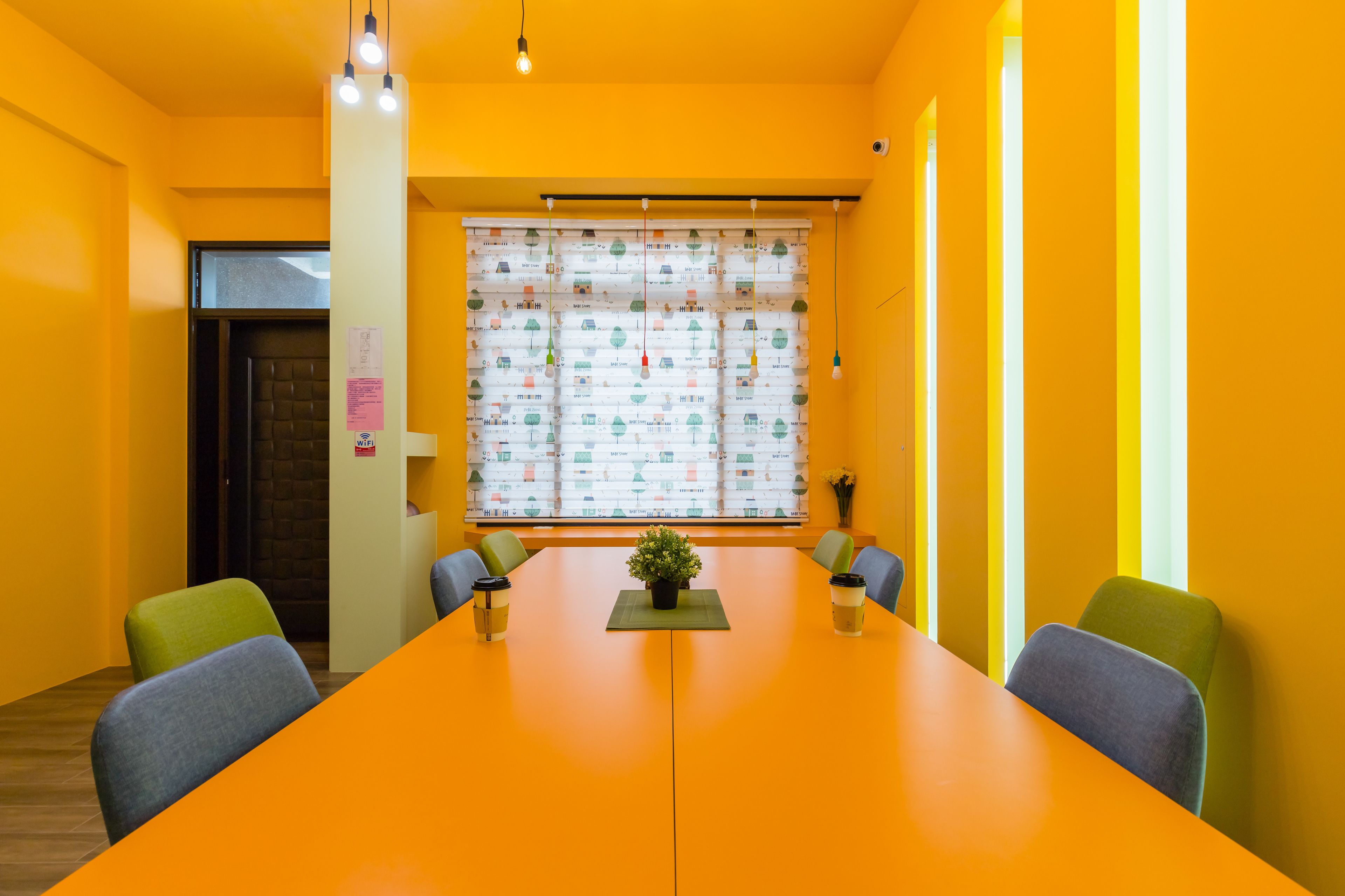 A conference room with a long table, chairs, a potted plant, and a window with blinds.
