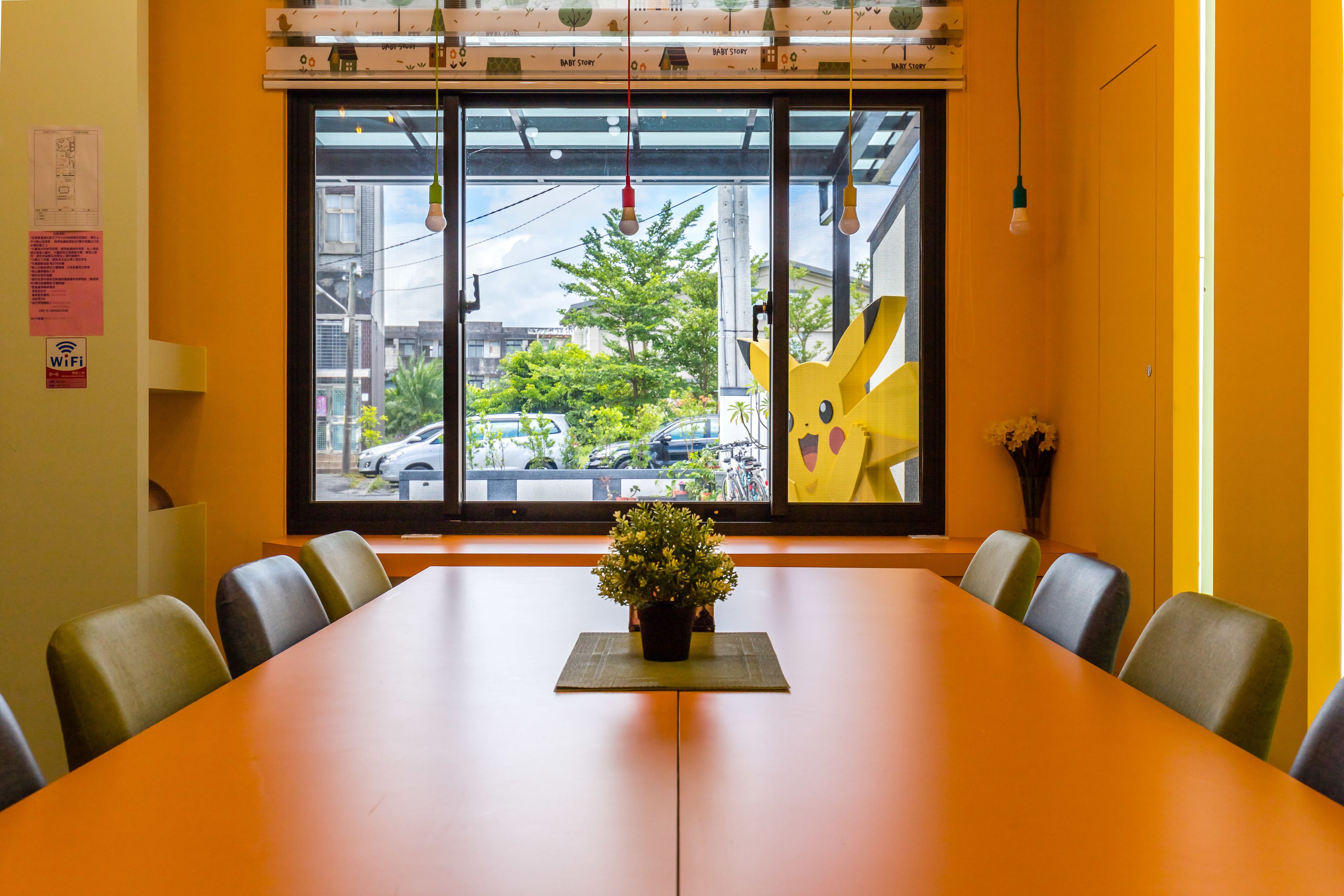 Un salón de conferencias con una mesa larga, sillas, una planta en maceta y un amplio ventanal con vistas al exterior.