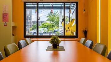 Un salón de conferencias con una mesa larga, sillas, una planta en maceta y un amplio ventanal con vistas al exterior.