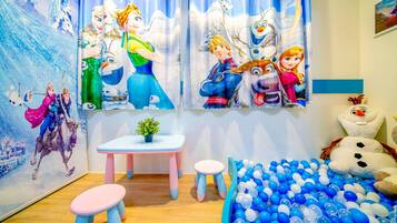 Un salón de juegos infantiles con una piscina de pelotas, una pequeña mesa, dos taburetes y una pared decorada con personajes de la película Frozen.