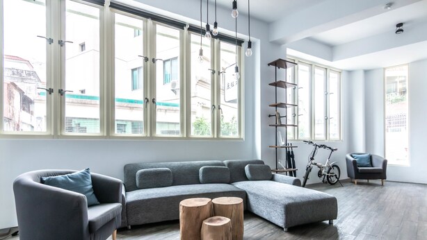 Uma sala de estar moderna com um sofá seccional, banquinhos de madeira e uma bicicleta ao fundo.