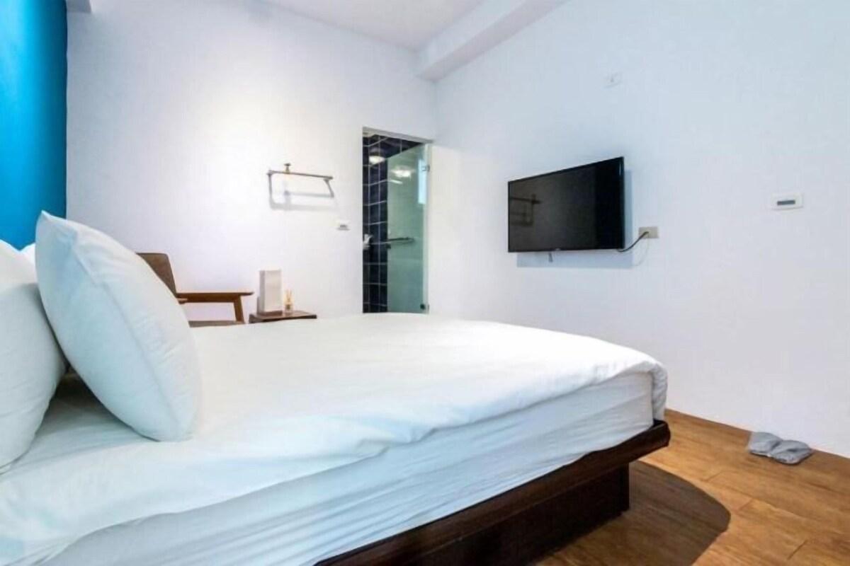 Ein modernes Hotelzimmer mit einem großen Bett, einem an der Wand befestigten Flachbildfernseher und einem kleinen Nachttisch.