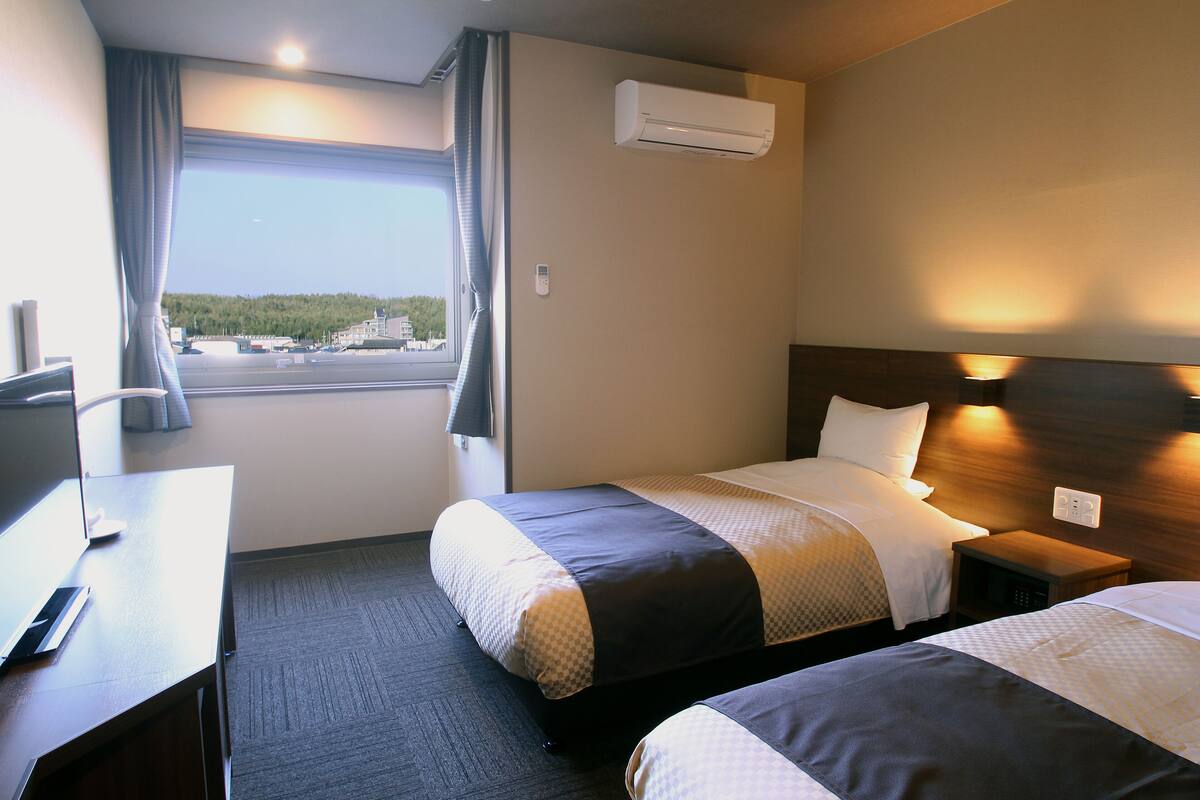 Ett hotellrum med två sängar, ett skrivbord och ett fönster med gardiner.