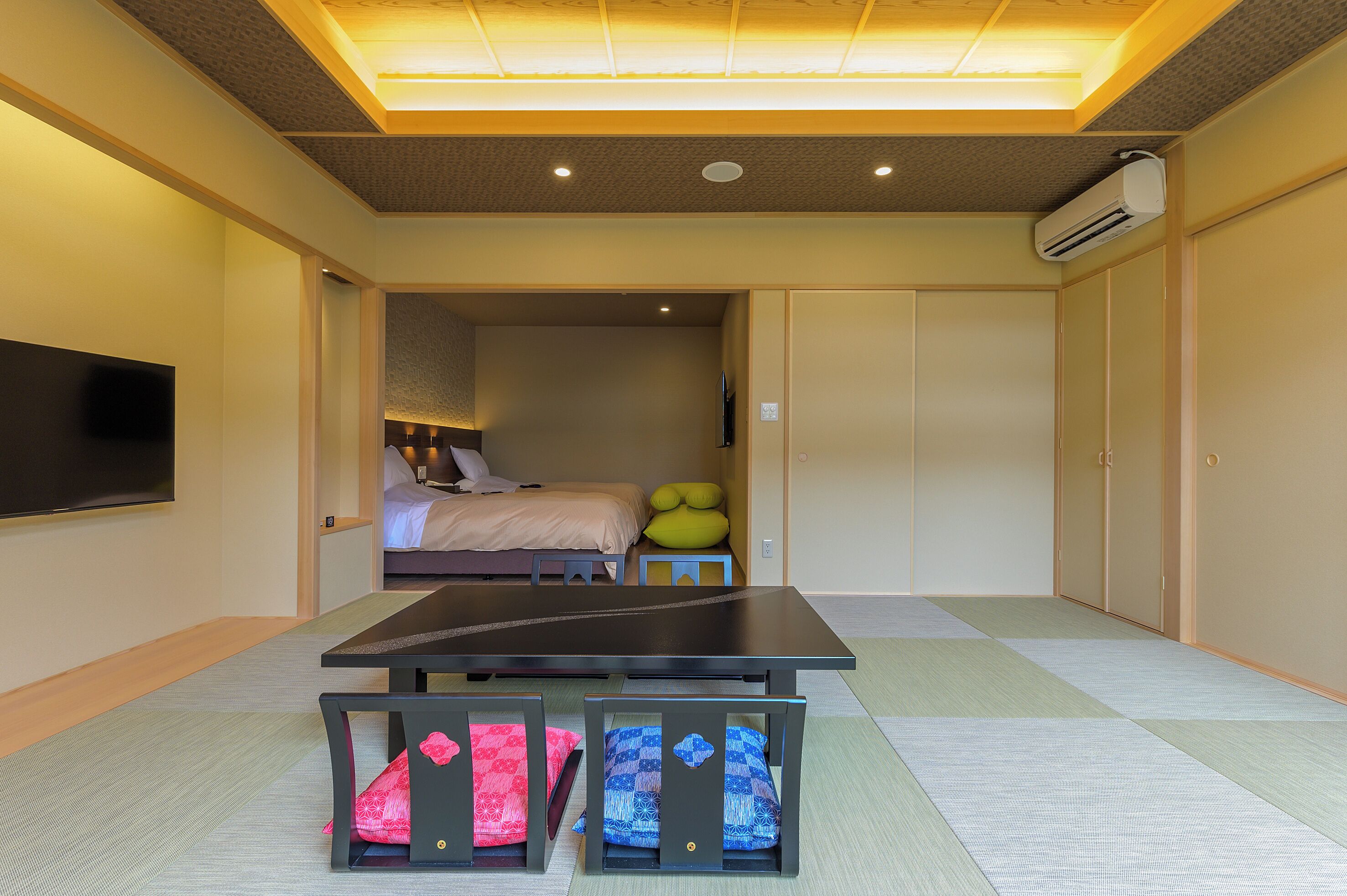 A hotel room with a bed, a TV, a table, and a futon.
