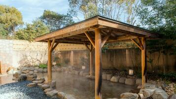 A wooden gazebo with a stone floor and a stone wall in the background.