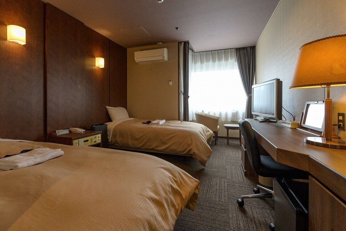 Ett hotellrum med två sängar, ett skrivbord med en dator, en stol, en tv och en luftkonditioneringsanläggning.