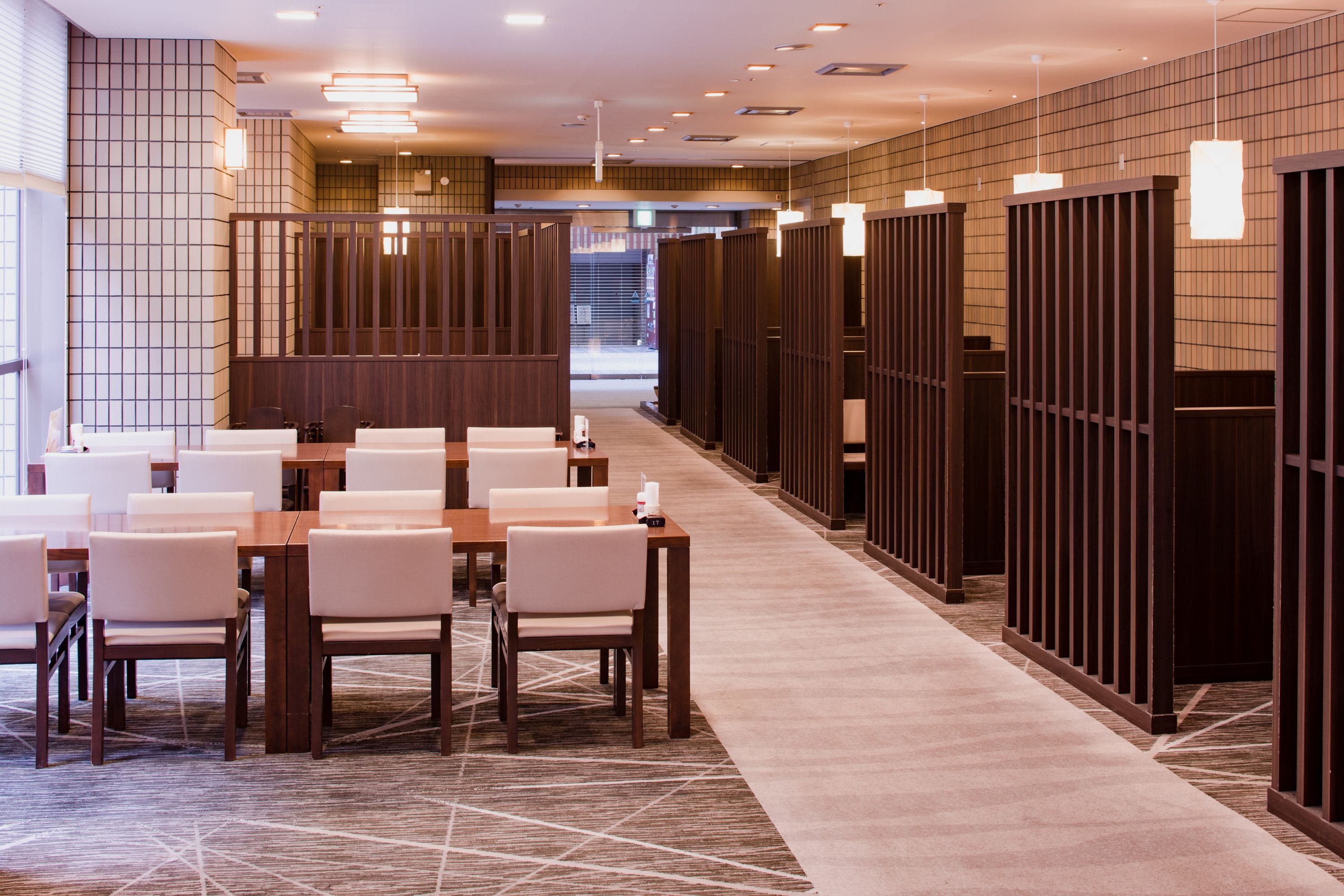 A hotel lobby with a long reception desk, multiple seating areas, and a corridor leading to private rooms.