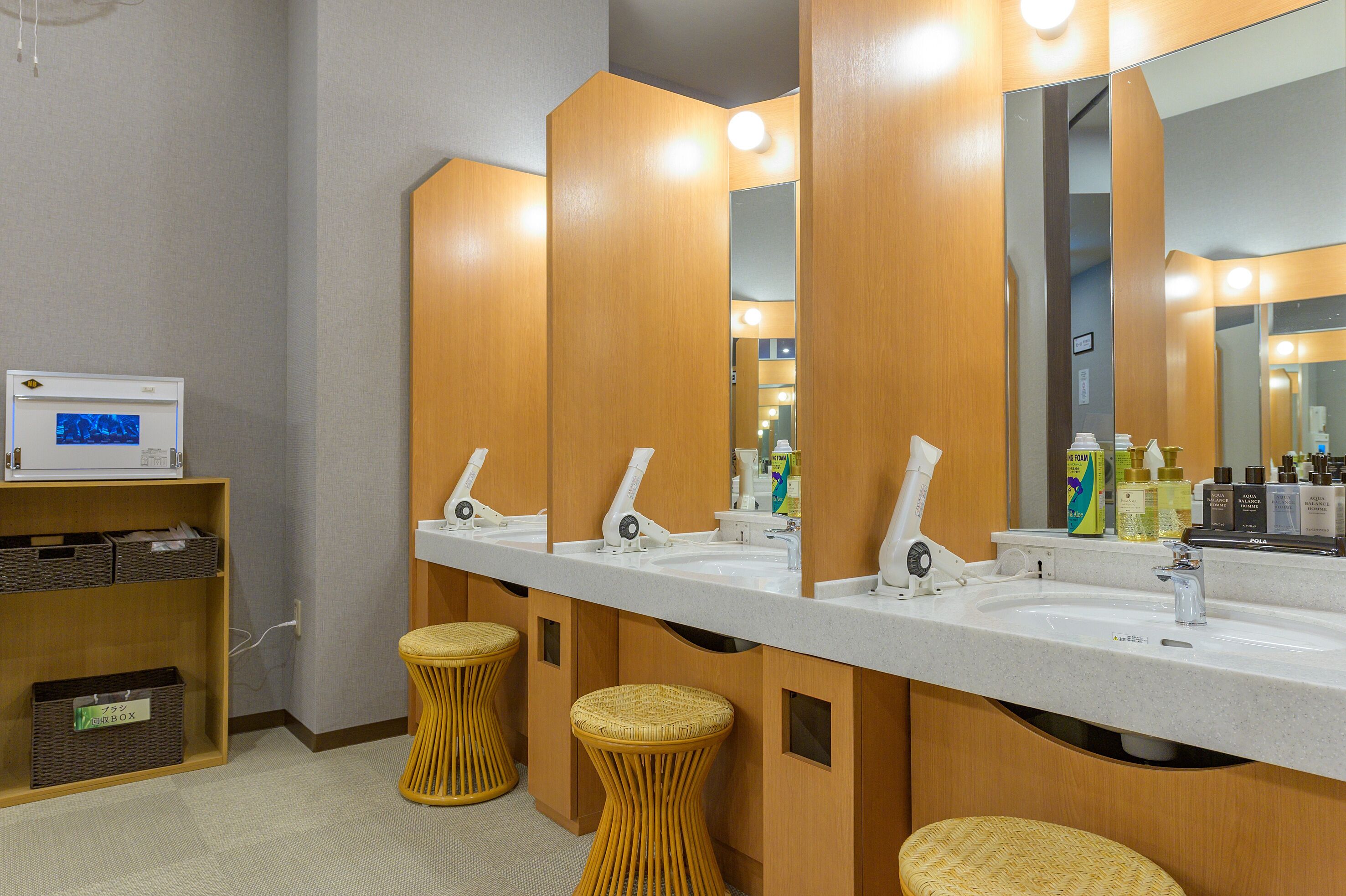 A modern bathroom with three sinks, a large mirror, and wicker stools.