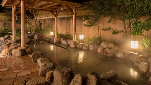 Een warmwaterbrongebied met een houten kiosk, een pad van stenen en rotsen rondom het water.
