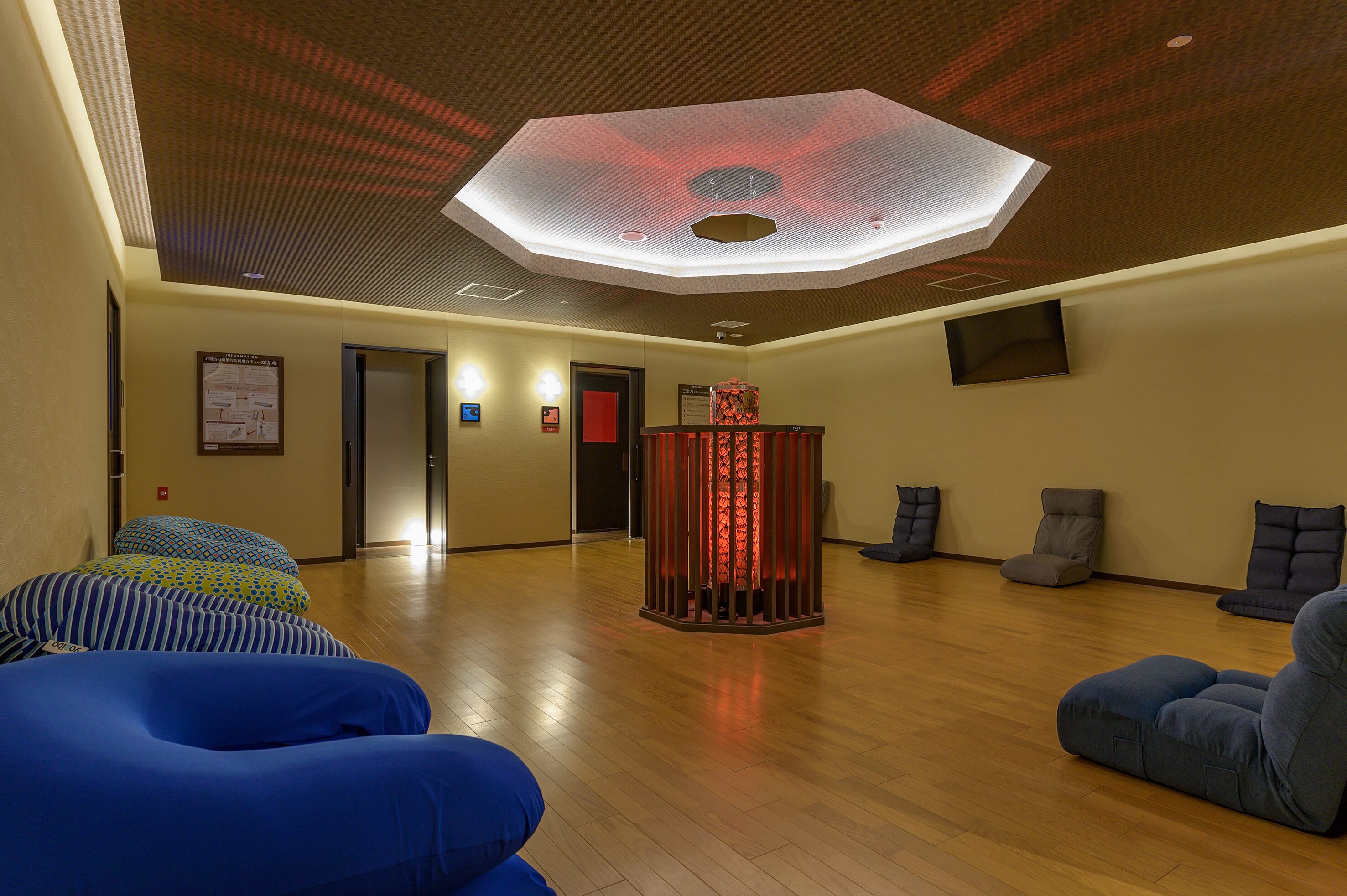 Une pièce spacieuse dotée d’un plancher en bois, d’une colonne centrale illuminée de lumière rouge et d’un plafond agrémenté d’un luminaire aux formes géométriques.