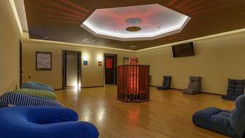 Une pièce spacieuse dotée d’un plancher en bois, d’une colonne centrale illuminée de lumière rouge et d’un plafond agrémenté d’un luminaire aux formes géométriques.