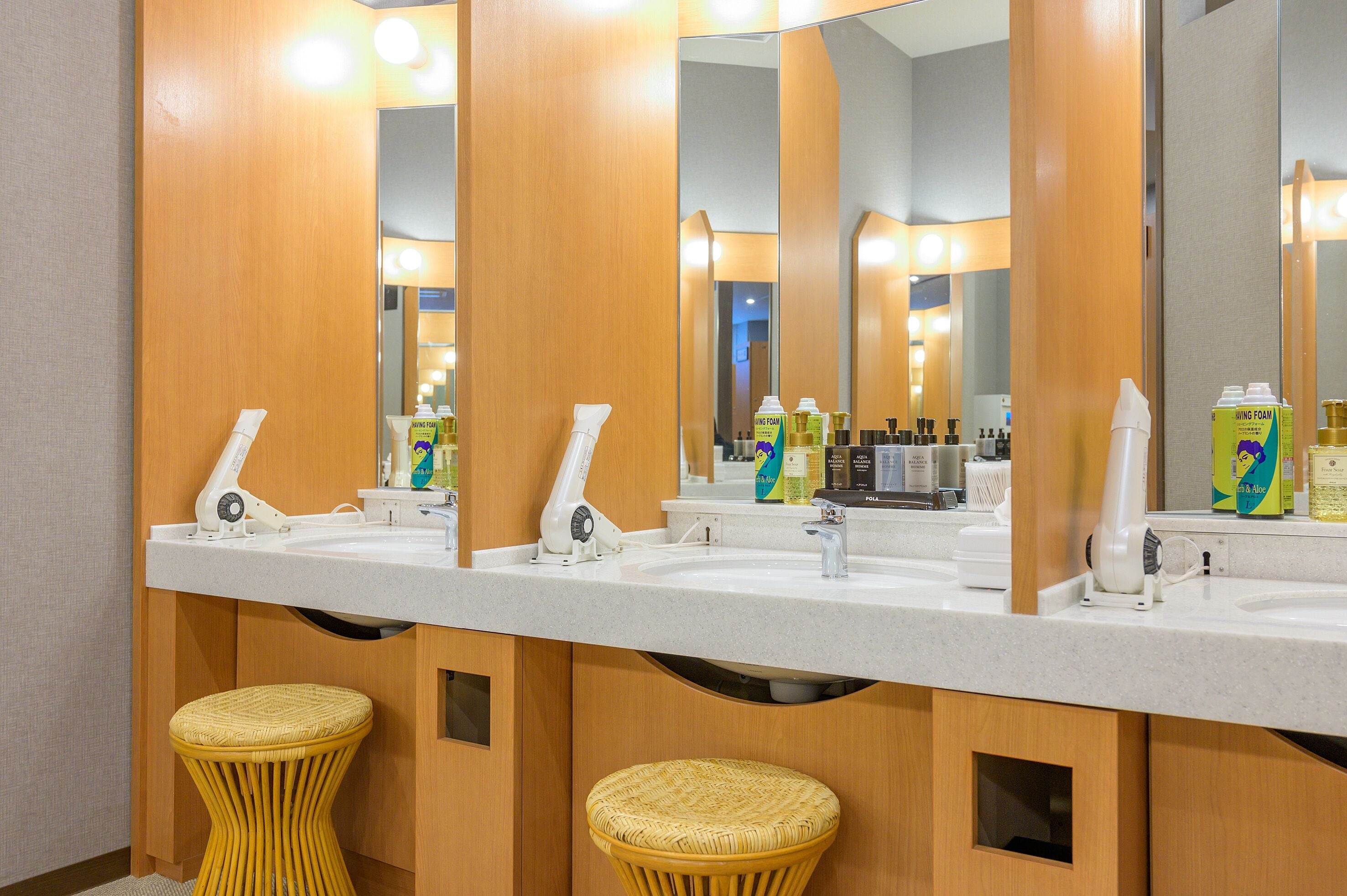 A hotel bathroom with three sinks, mirrors, and two wicker stools.