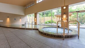 Een ruim binnenzwembad met een jacuzzi, betegelde wanden en grote ramen met uitzicht op het omliggende landschap.