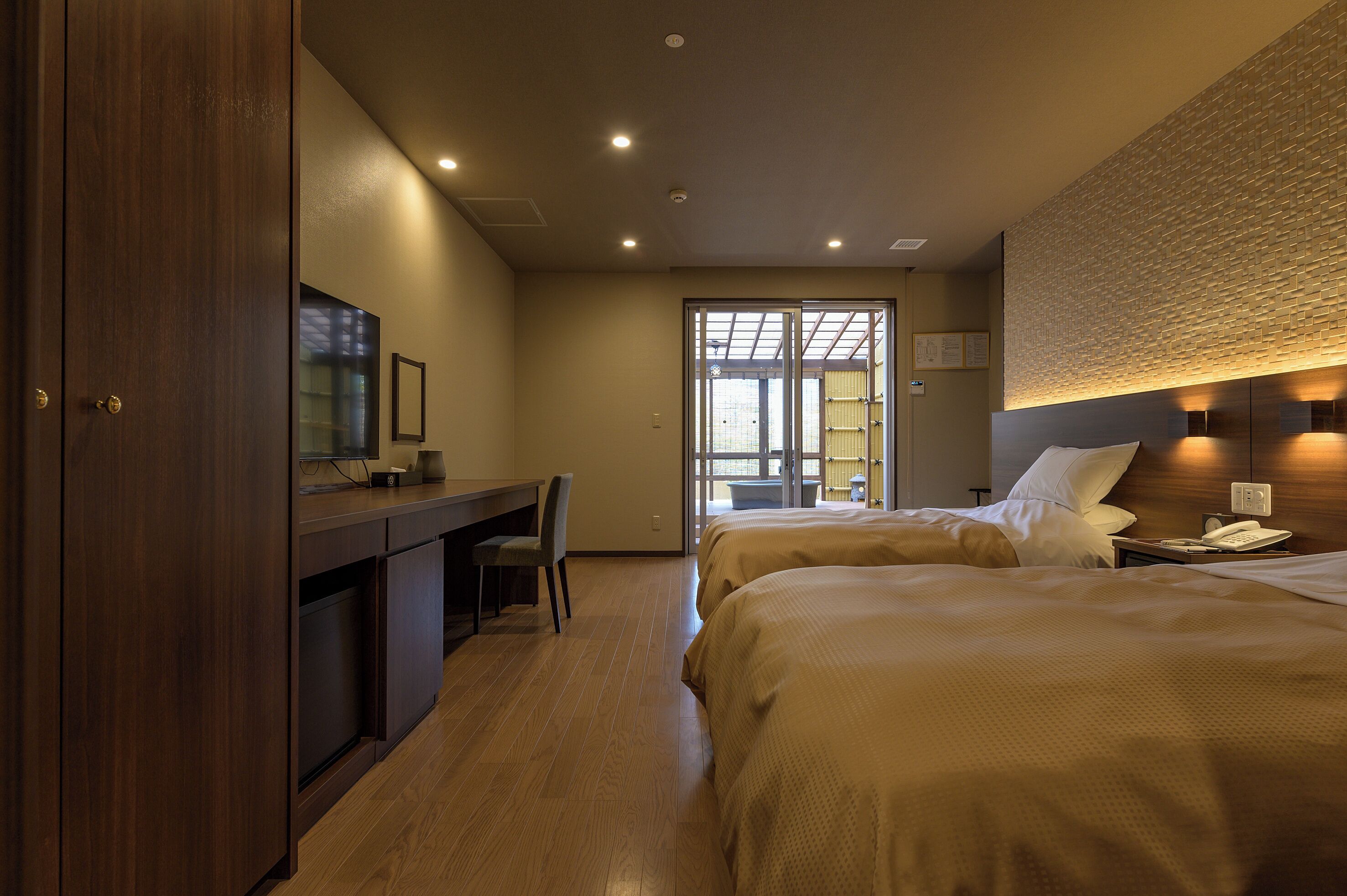 A hotel room with two beds, a desk, and a TV.