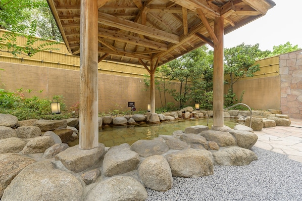 Una pérgola de madera sobre un estanque de peces koi, rodeado de rocas y guijarros.