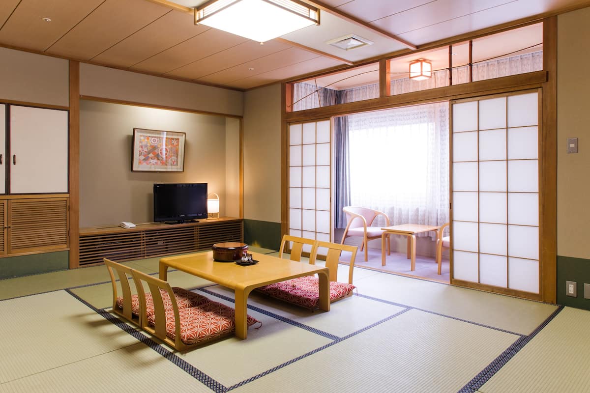 Ett traditionellt japanskt rum med tatamimattor på golvet, ett lågt träbord och en tv som står på ett stativ.
