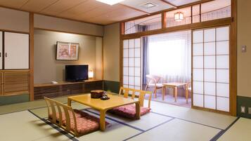 Una habitación japonesa tradicional con suelo de tatami, una mesa de madera baja y un televisor sobre un soporte.