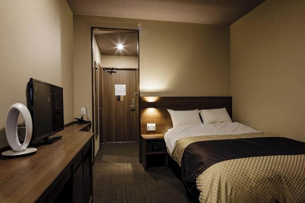 Ett hotellrum med en säng, ett nattduksbord, en tv och en ringlampa.
