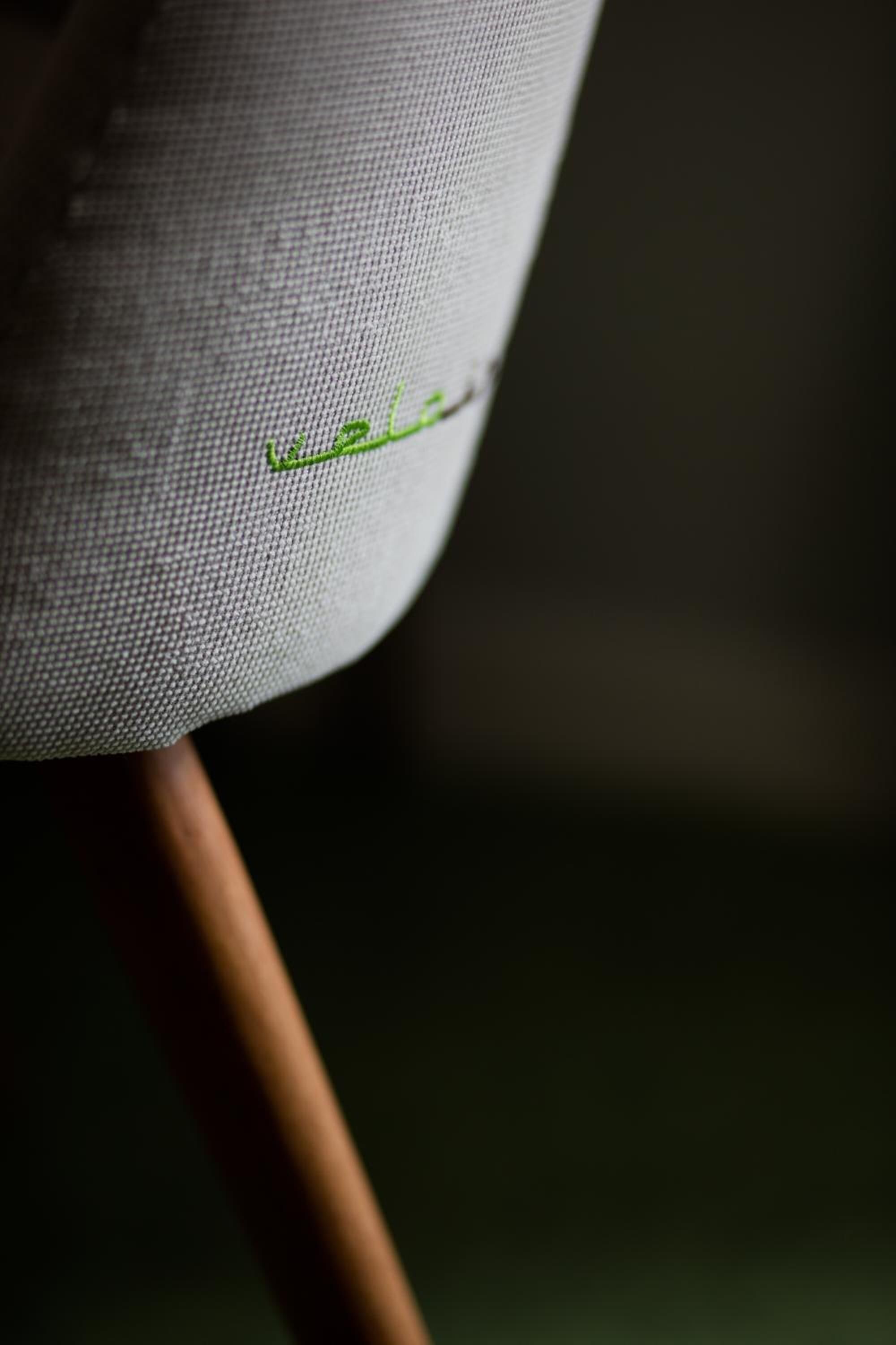 Un gros plan d’une chaise dont l’assise est recouverte d’un tissu et qui présente un détail brodé de couleur verte.