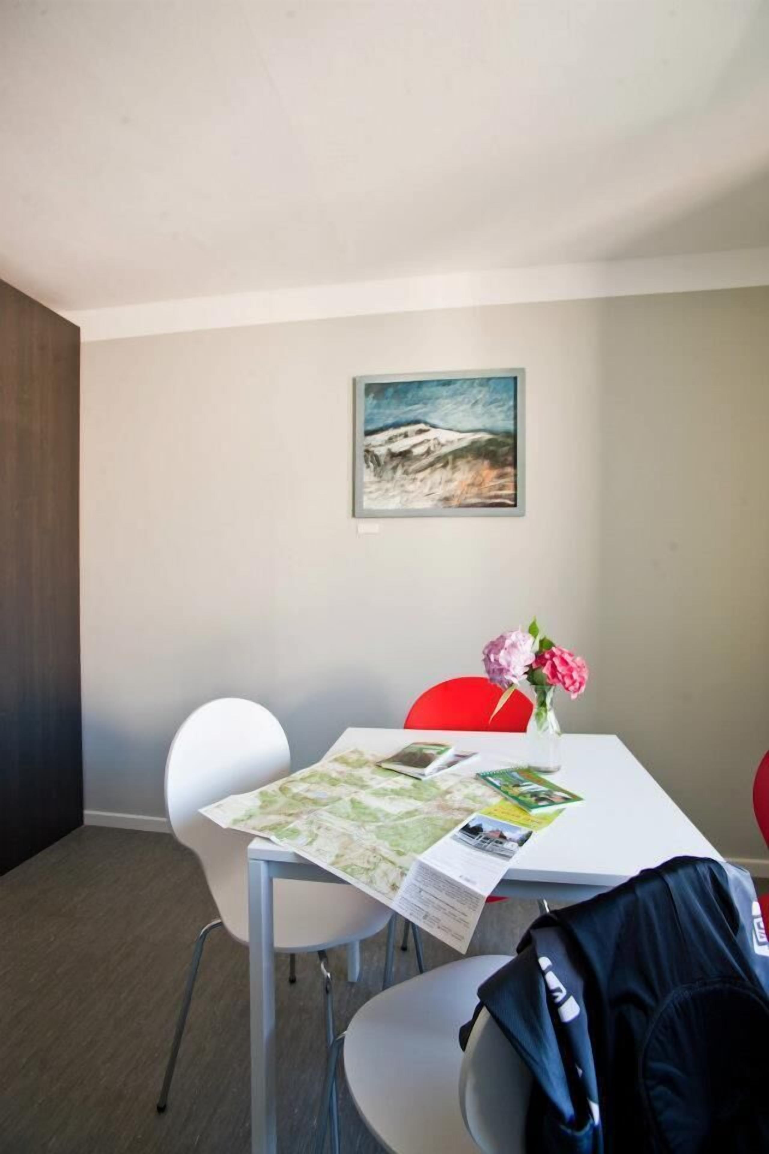 A dining area with a table set for two, a map, and a vase with flowers.