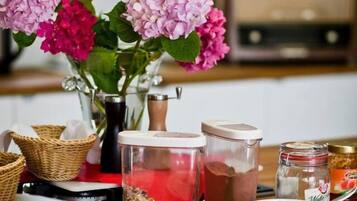 Ein Tisch mit verschiedenen Speisen, darunter Obst, eine Schüssel Müsli und eine Vase mit Blumen.