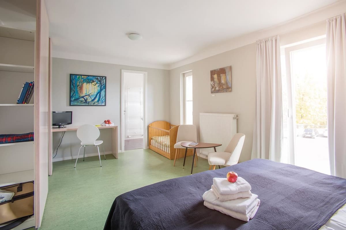 Hotellihuone, jossa on sänky, työpöytä, tuoli, vauvansänky ja kirjahylly.