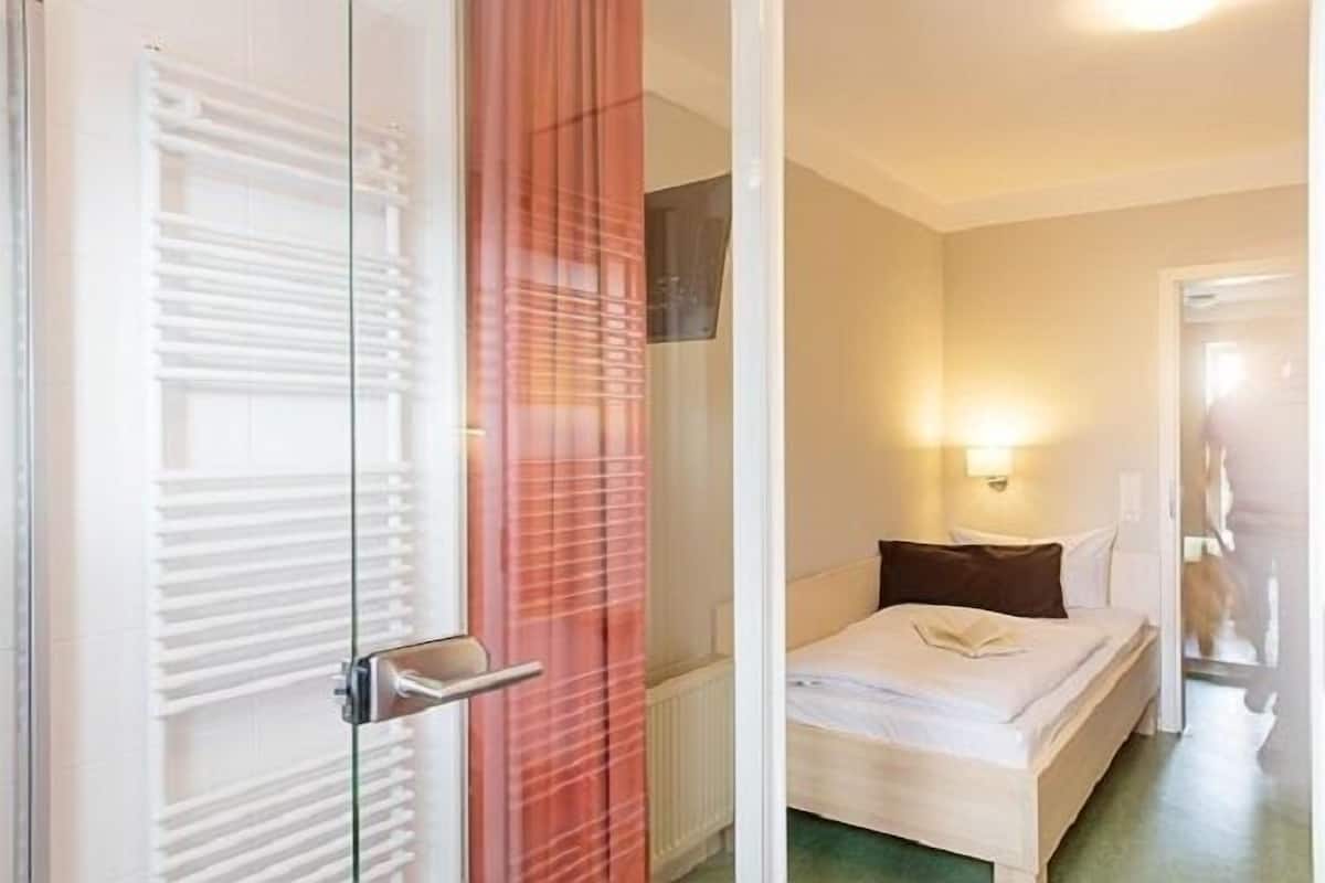 Hotellihuone, jossa on sänky, yöpöytä, seinään kiinnitetty valaisin ja liukuovi, jossa on pyyheteline.