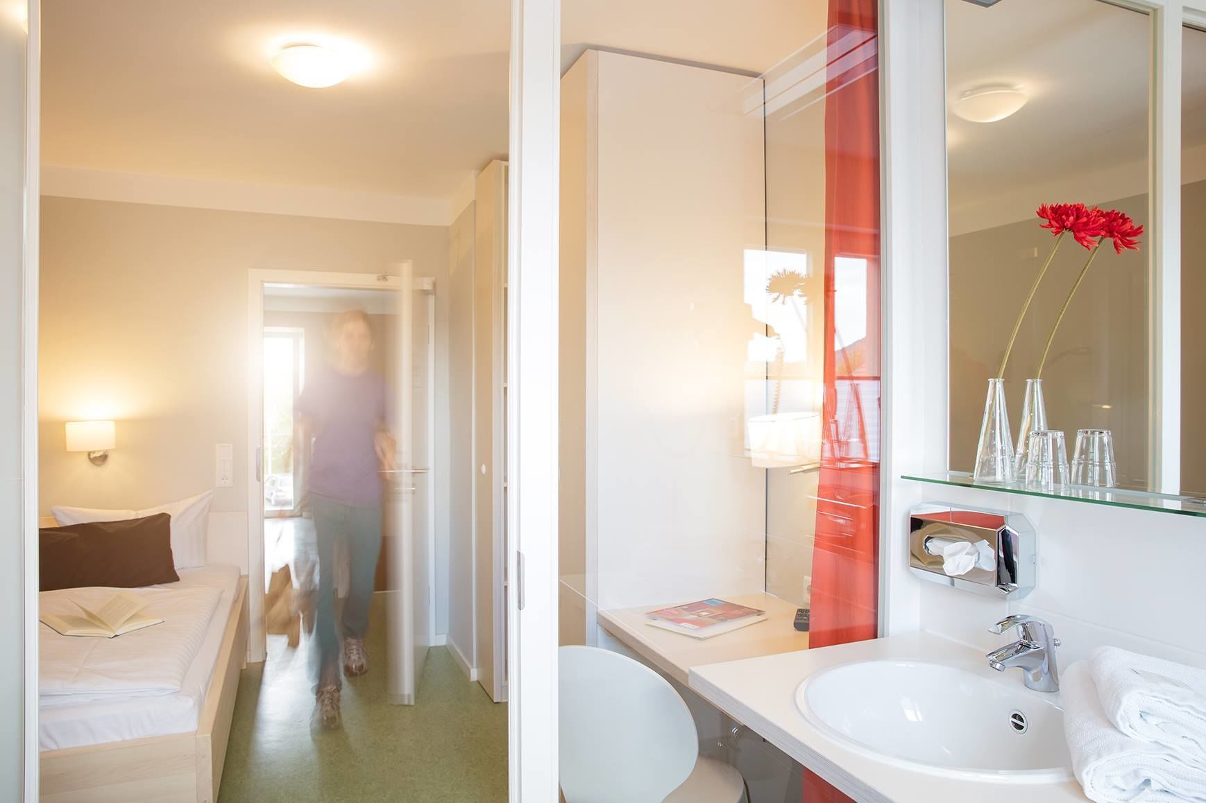Ein Hotelzimmer mit einem Bett, einem Nachttisch, einem Spiegel, einem Waschbecken und einer Toilette.