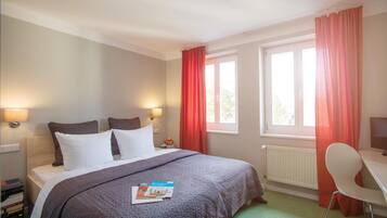 Una habitación de hotel con cama, dos lámparas de noche, un escritorio con silla y una ventana con cortinas.