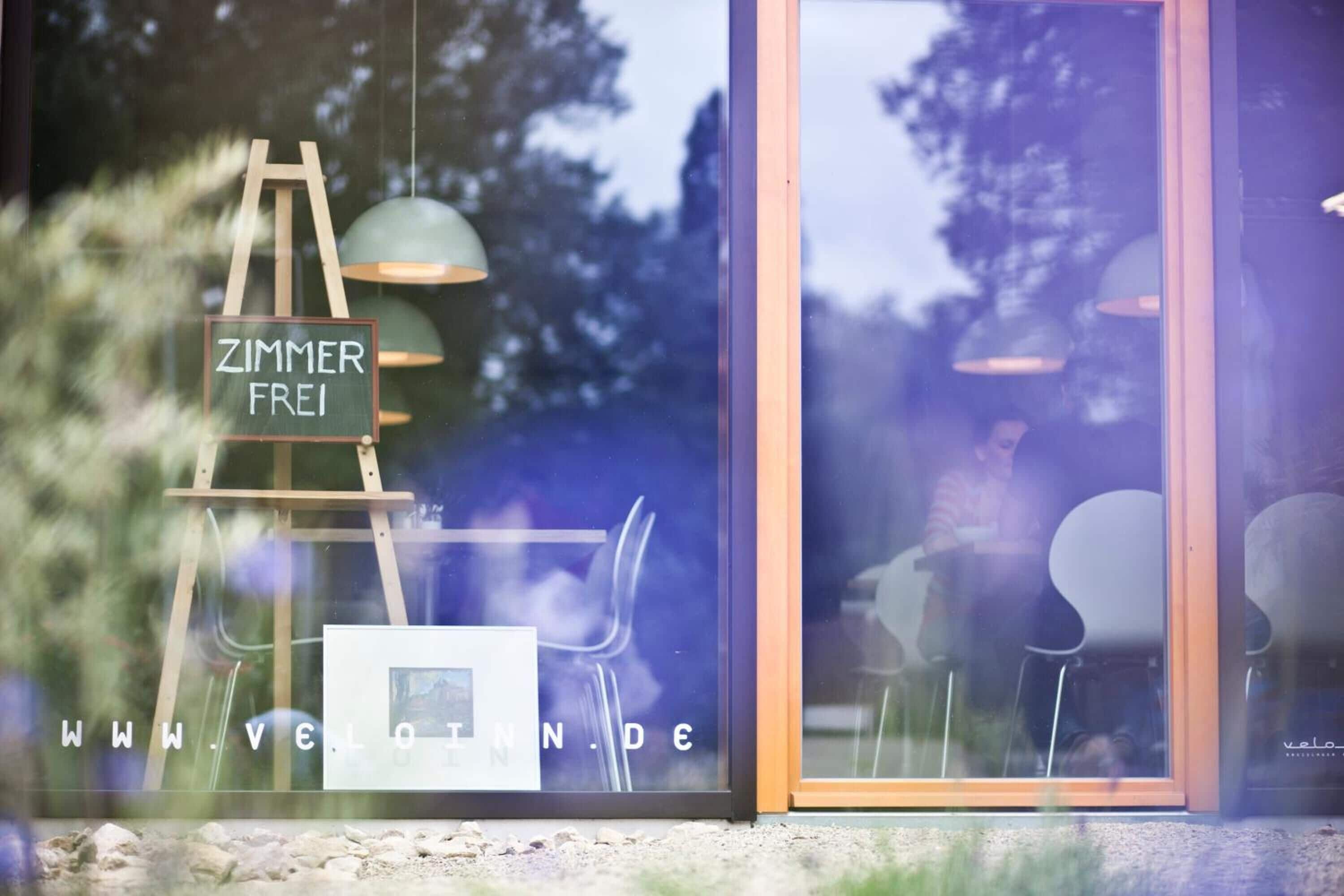 Ein Fenster mit einem Schild, das "ZIMMER FREI" zeigt, und einer Website-Adresse "WWW.VELOTINDE".