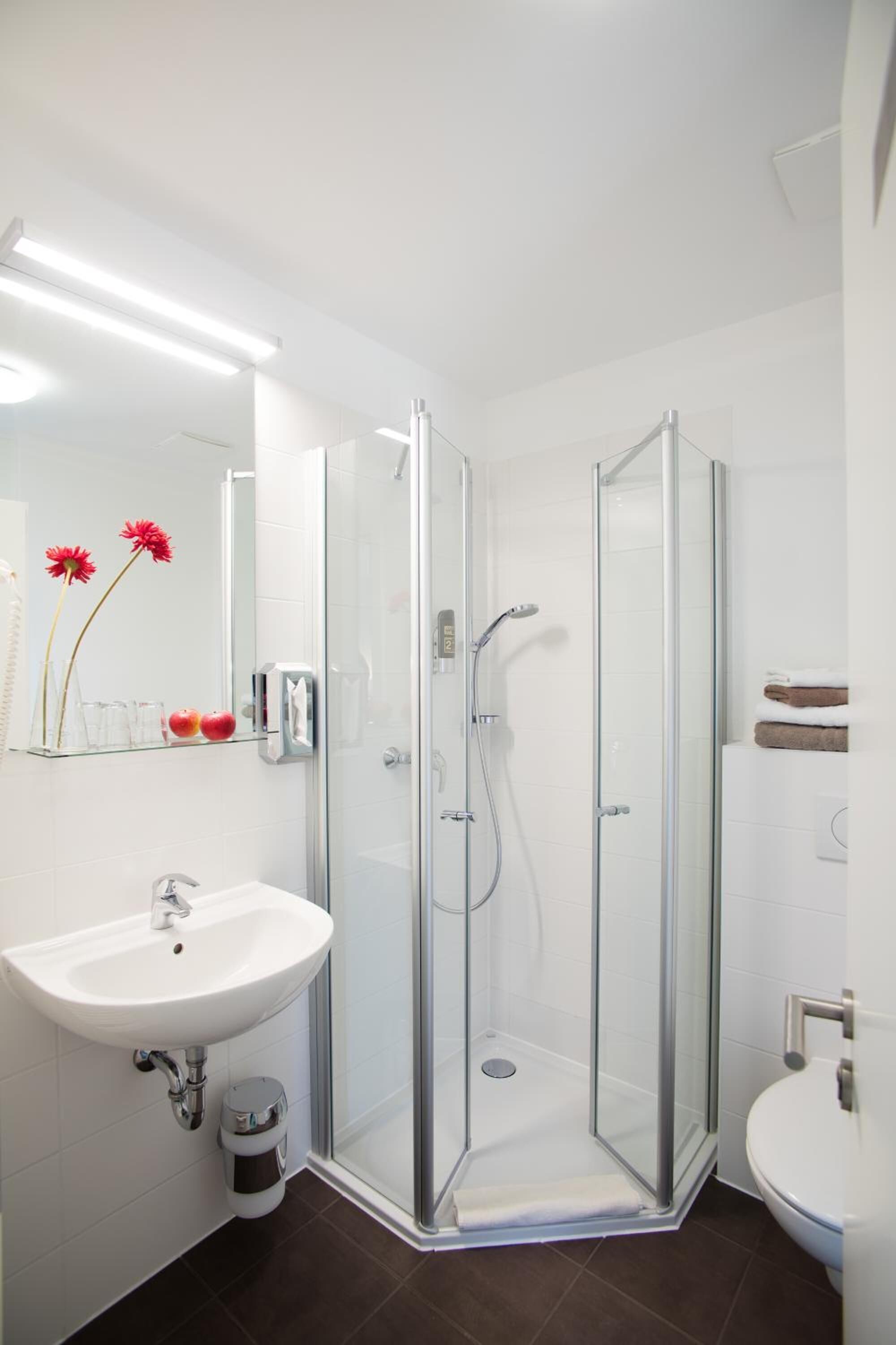 Une salle de bain moderne avec une douche à parois de verre, un lavabo blanc et un miroir décoré de fleurs.